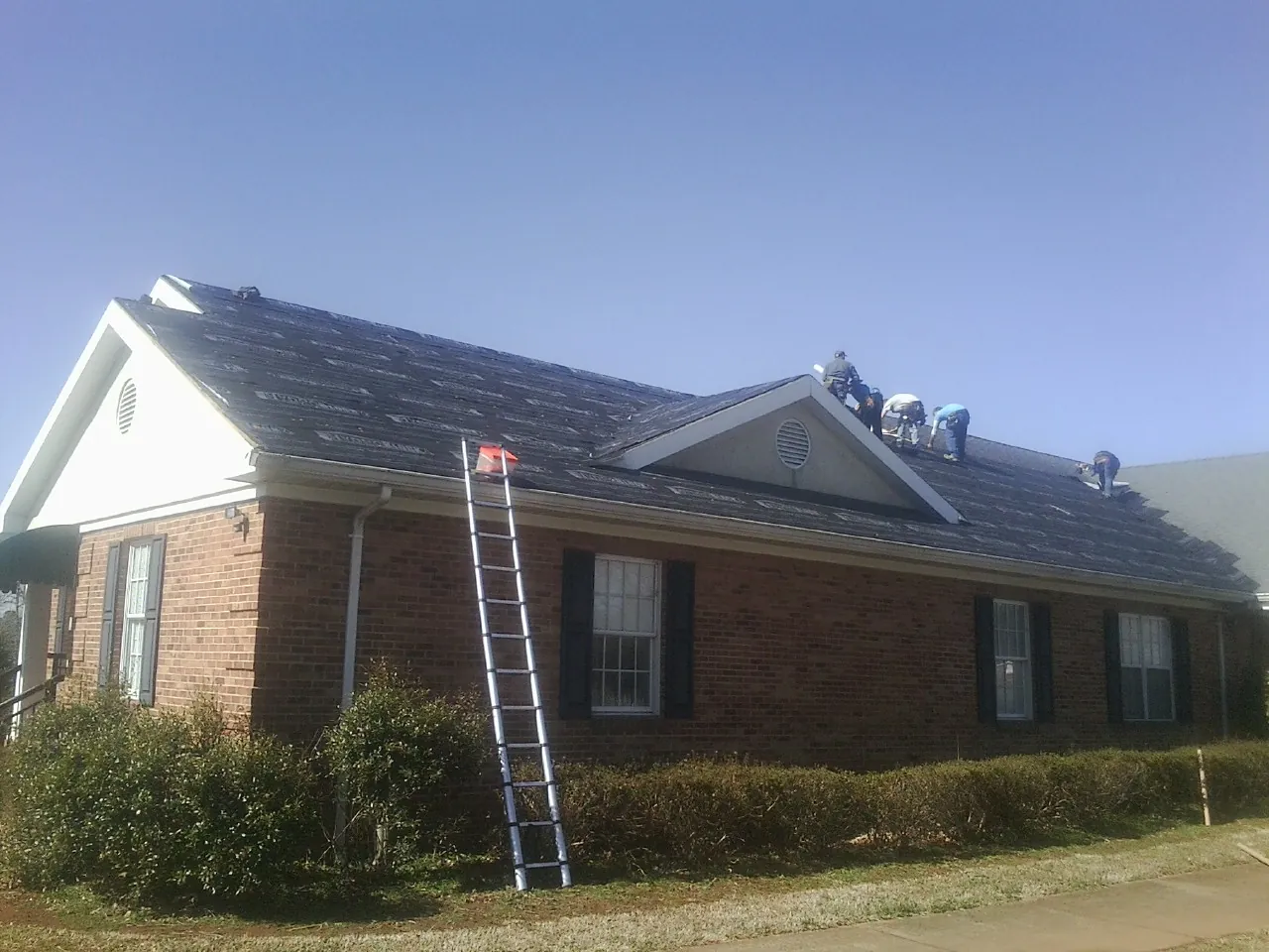Crew tearing shingles off a brick ranch roof with a ladder set — Emergency Roof Repair work by our crew in South Chatham