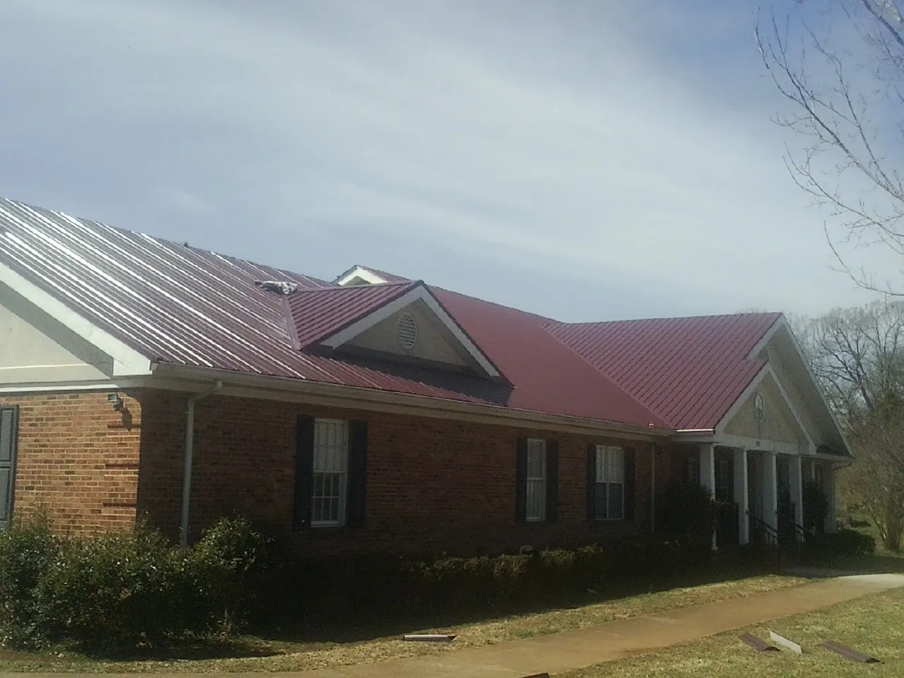 Red metal roof with gabled entries on a long brick building, from a Hail Damage Roof Repair job in South Chatham