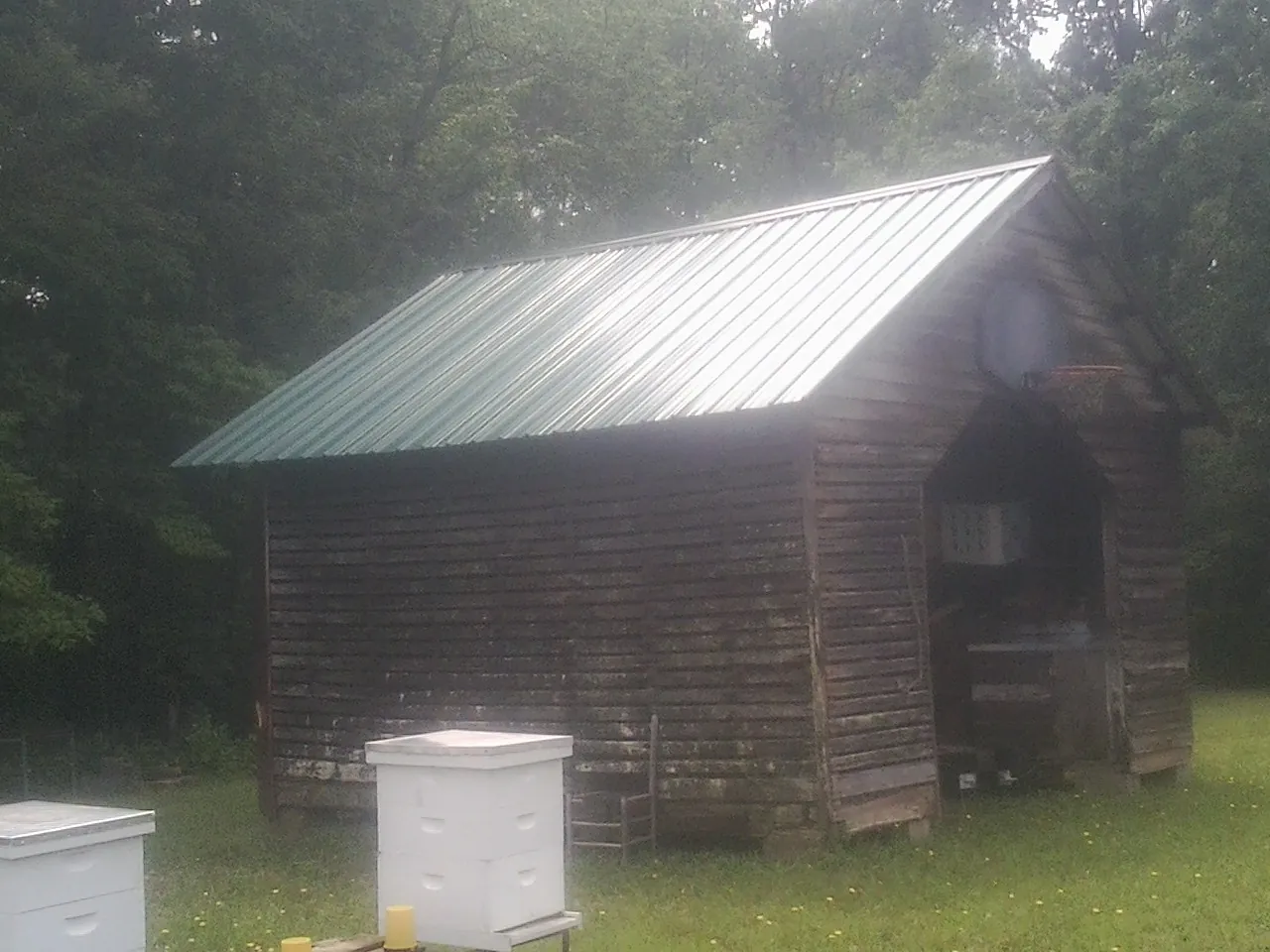 Green metal roof on a weathered barn beside stacked beehives in South Chatham
