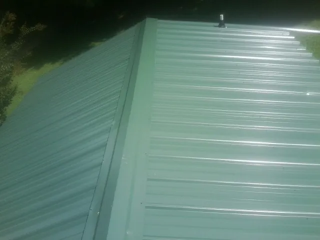 New green metal panels meeting at the ridge of a roof — Flat Roof Repair work by our crew in South Chatham
