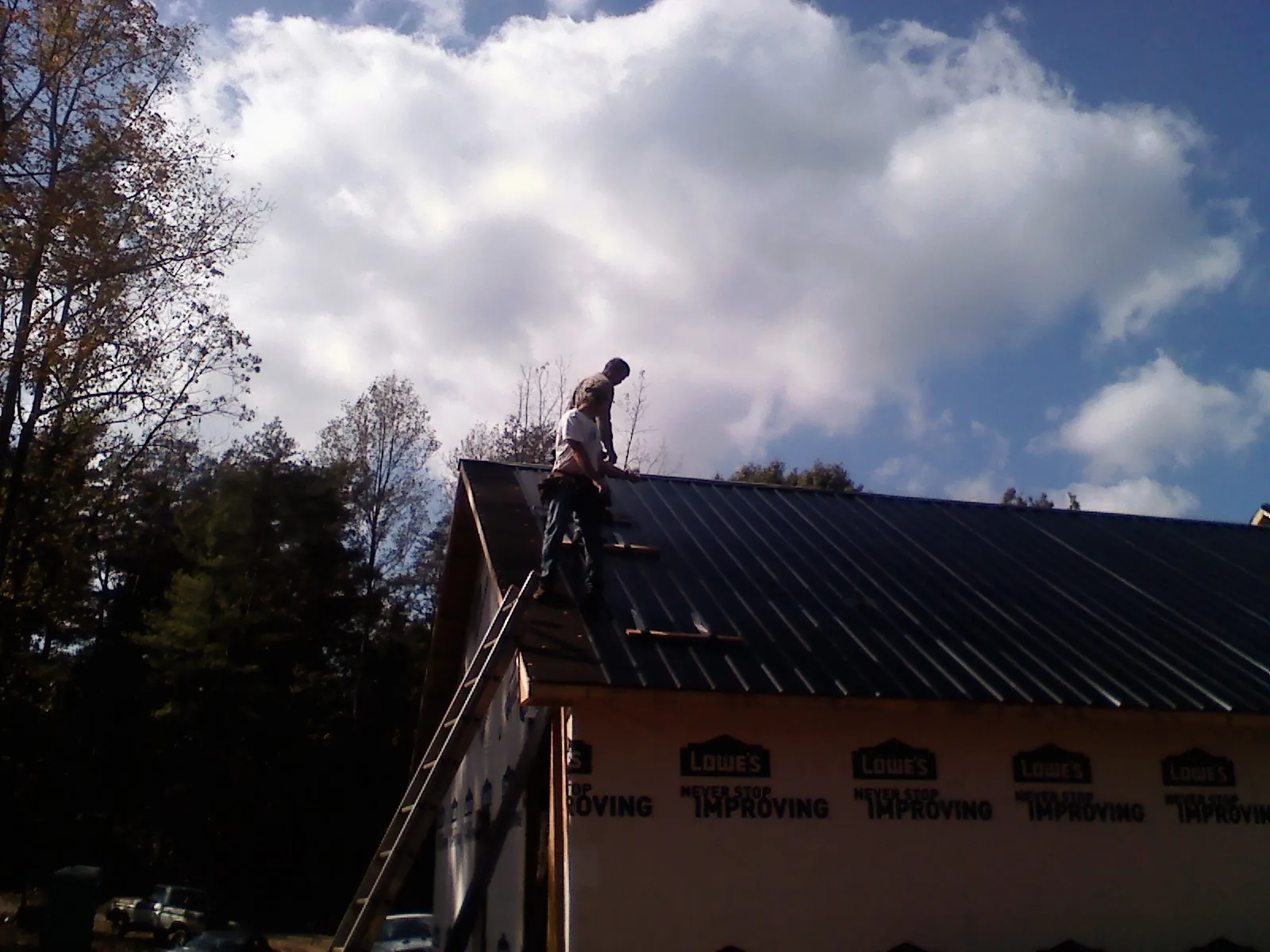 Roofer fastening dark metal panels high against a cloudy sky, from a Roof Inspection job in South Chatham