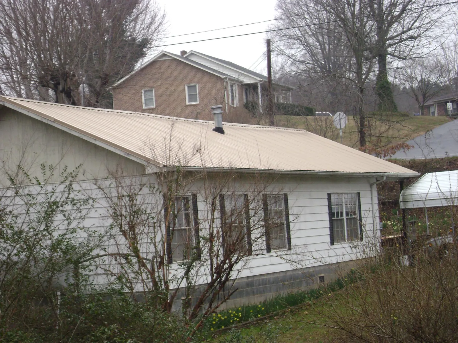 Tan metal roof on a white sided house set into a hillside — Commercial Roofing by Roofing Brothers in South Chatham